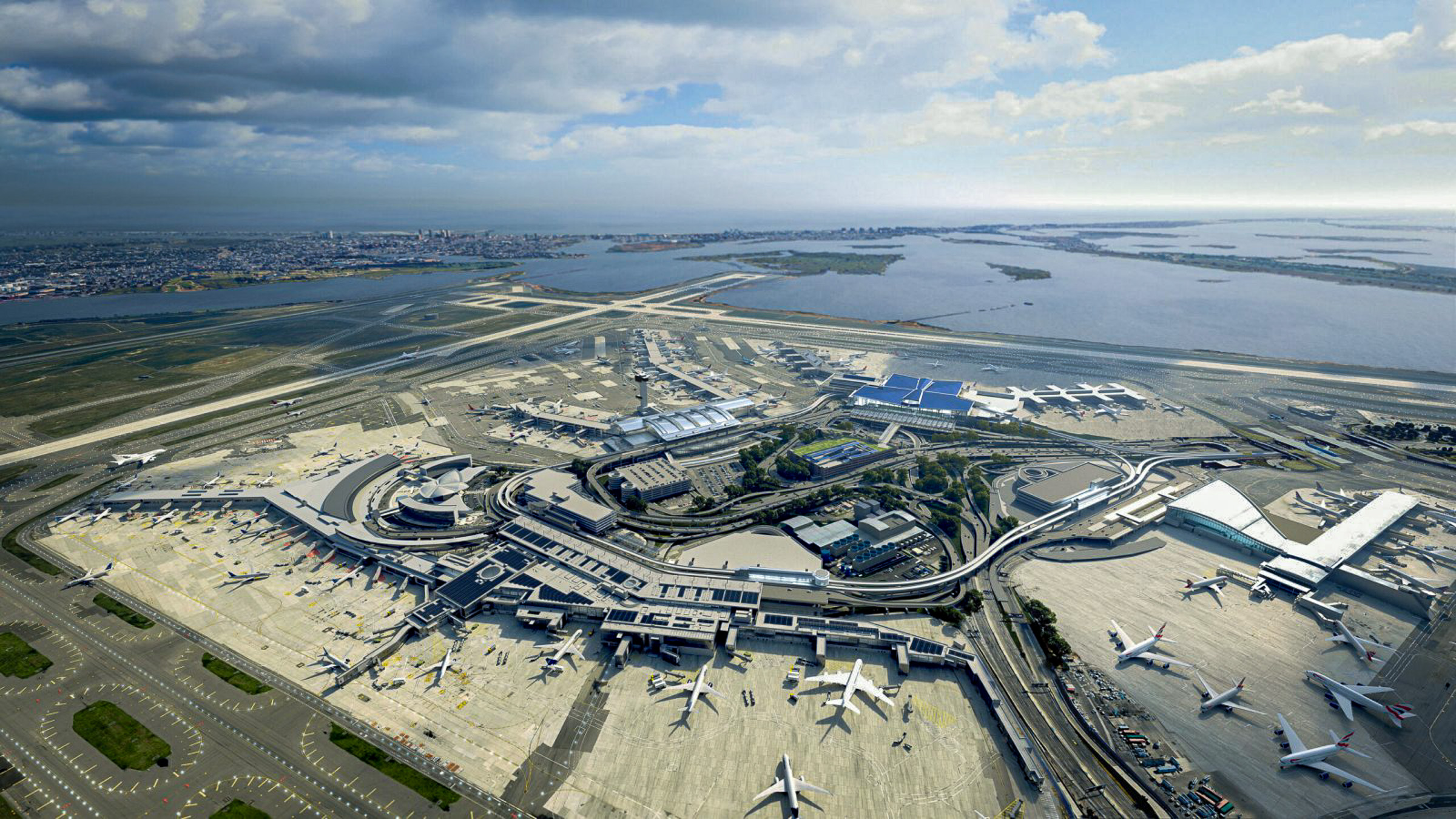 ภาพถ่ายทางอากาศมุมสูง (Aerial View) แสดงผังของอาคารผู้โดยสารในสนามบิน JFK ที่จัดเรียงเป็นวงแหวนรอบพื้นที่ส่วนกลาง และรันเวย์ตัดกันริมชายฝั่งทะเล